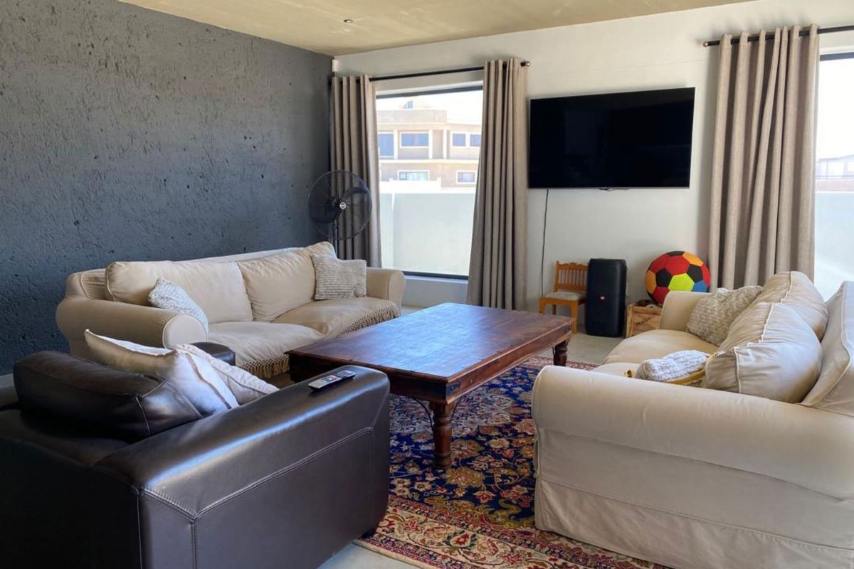A spacious living room featuring a textured accent wall, large windows with curtains, and recessed ceiling lighting.