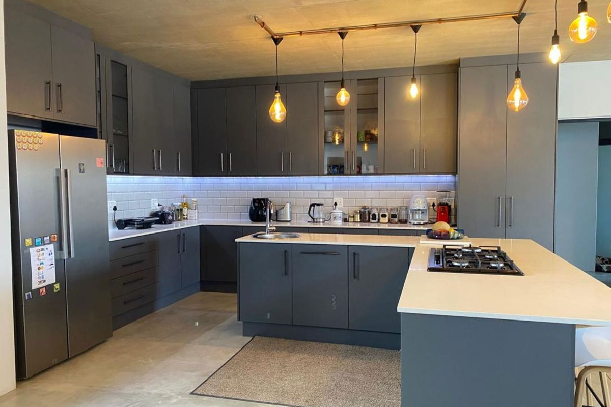 Modern kitchen featuring dark grey cabinetry, white stone countertops, a central island with a built-in gas hob, and industrial-style exposed copper lighting.