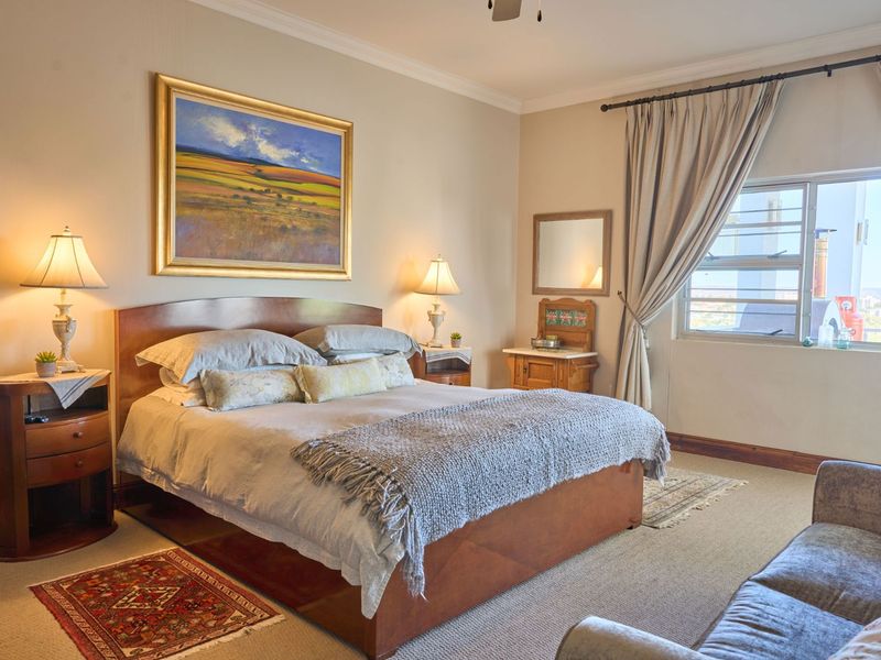A well-maintained bedroom featuring neutral wall tones, coving, and a large window providing natural light and exterior views.