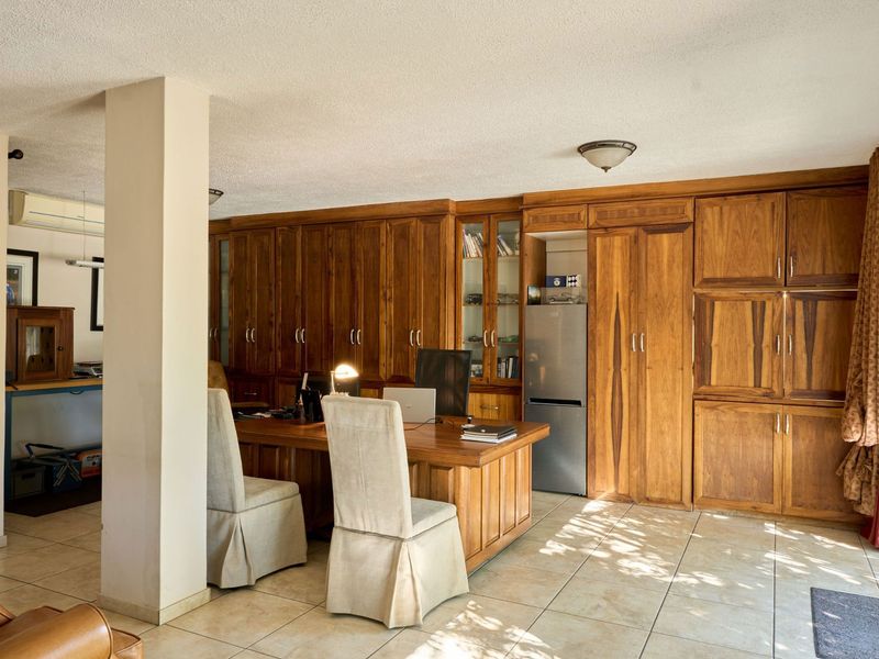 A home office featuring extensive built-in wooden cabinetry, tiled flooring, and a structural column, providing a functional workspace with integrated storage solutions.