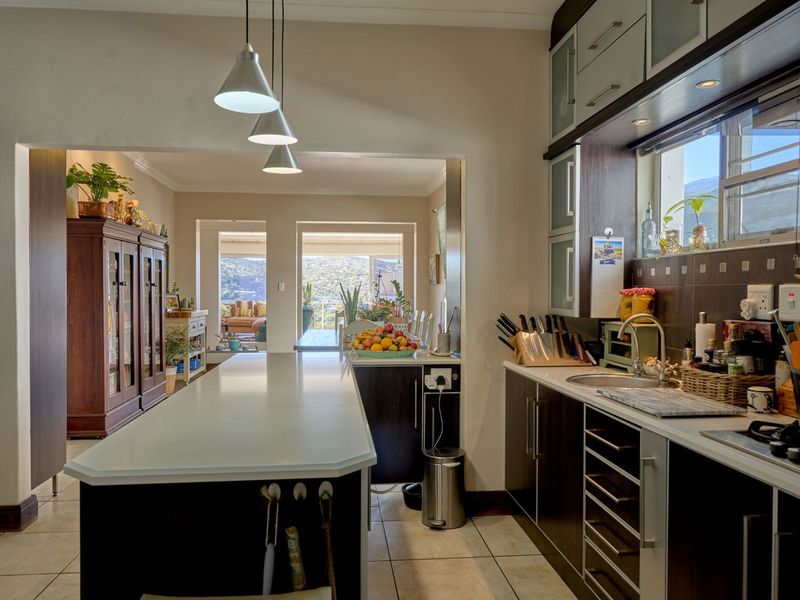 An open-plan kitchen featuring a central island, modern cabinetry, and tiled flooring, flowing seamlessly into the adjacent living area with scenic views.