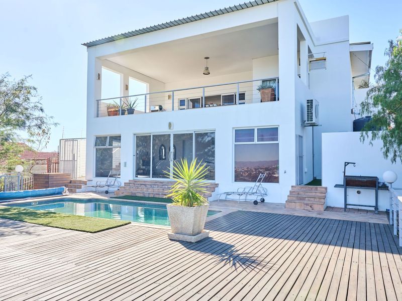 Rear exterior view featuring a swimming pool, timber decking, covered patio, and balcony, providing an ideal space for outdoor entertainment.