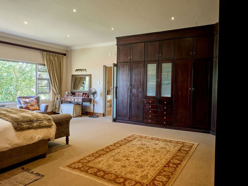 Spacious bedroom featuring extensive dark wood built-in cabinetry, neutral carpeting, recessed lighting, and a large window providing natural light.