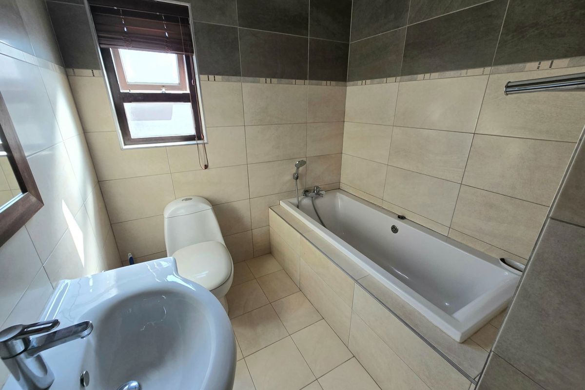 A modern bathroom featuring a built-in bathtub, a pedestal basin with chrome mixer tap, and a toilet, finished with neutral wall and floor tiling.
