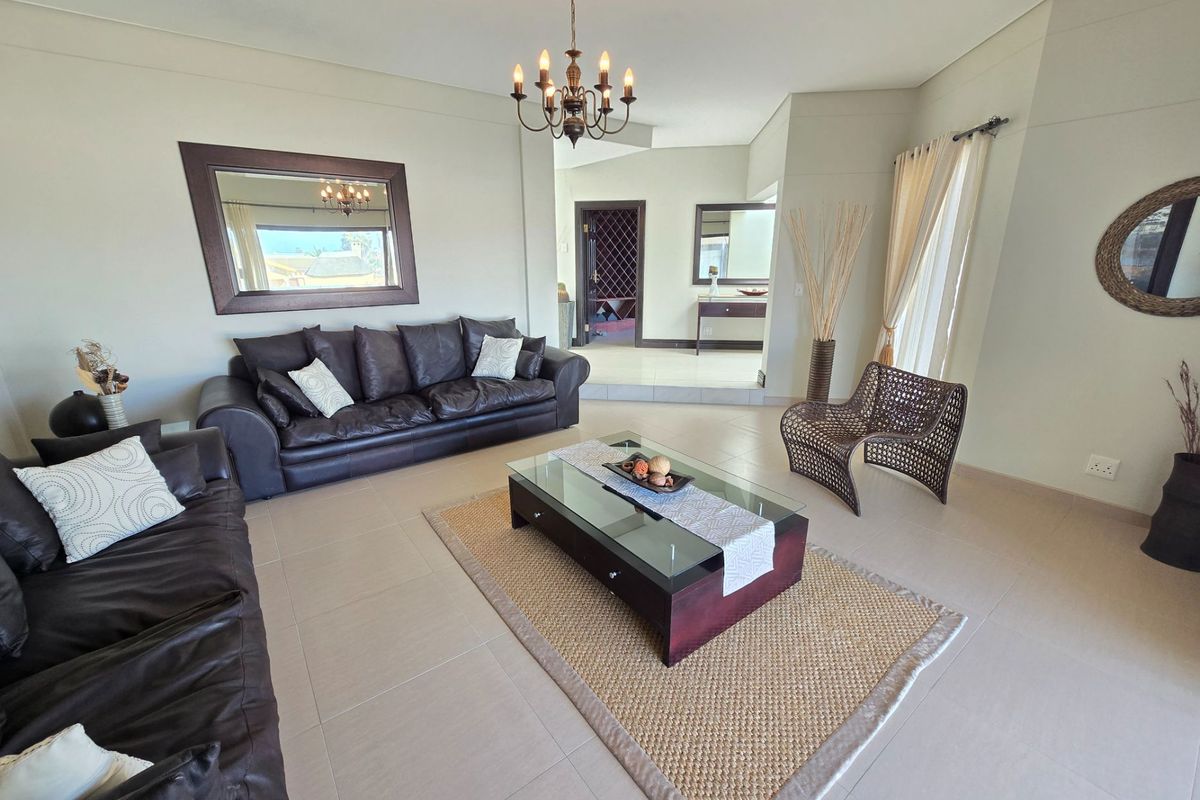 Spacious living room featuring neutral tiled flooring, a classic chandelier, and an open-plan layout leading to an adjacent area.