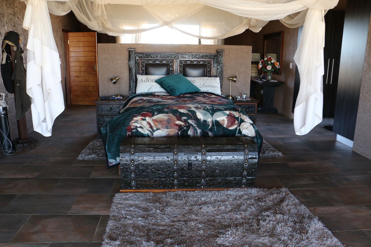 Spacious bedroom featuring dark tiled flooring, textured wall finishes, and a central bed area with integrated canopy structure.