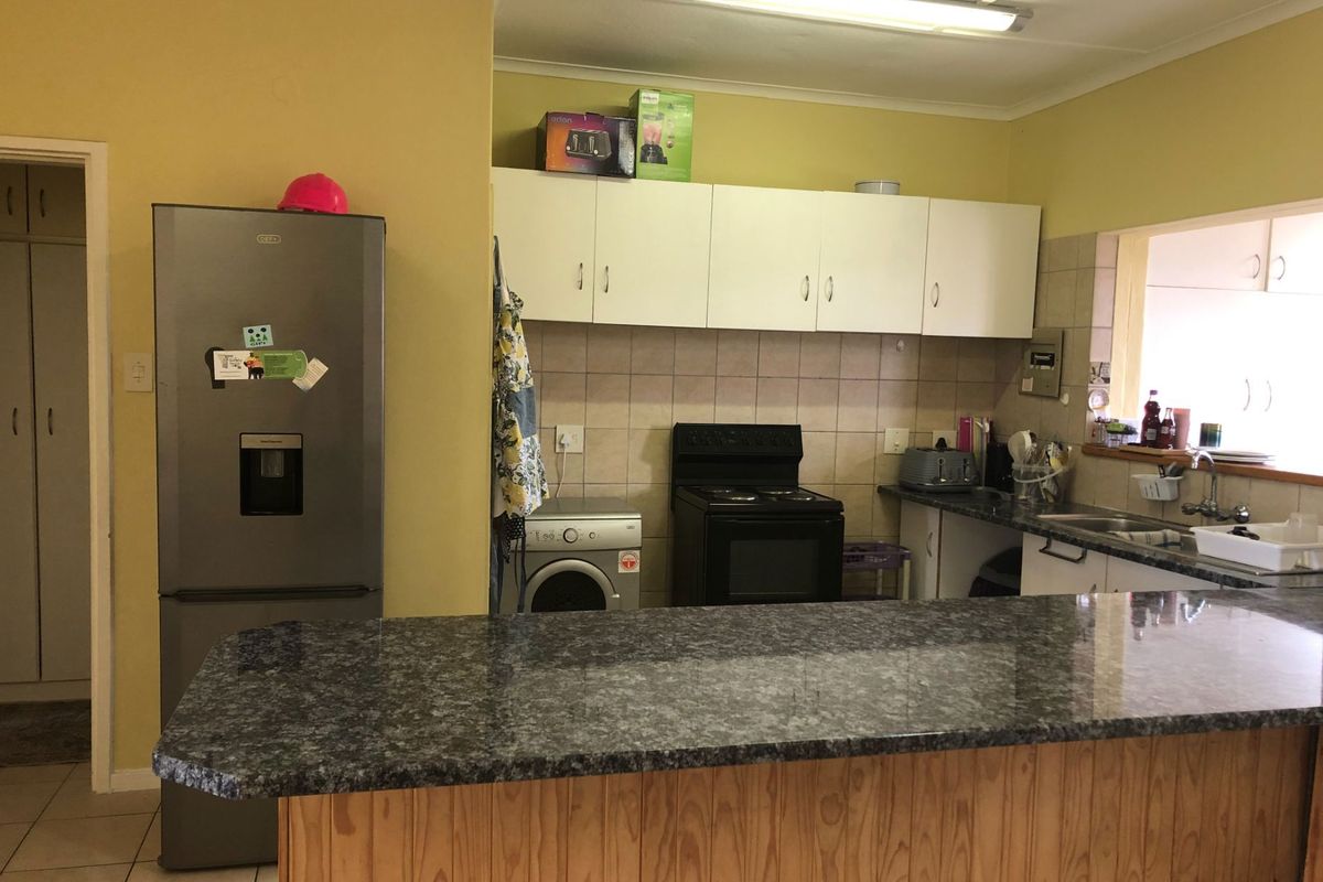Functional kitchen featuring a granite-look breakfast bar, white cabinetry, tiled splashback, and built-in stove, offering a practical layout for daily meal preparation.