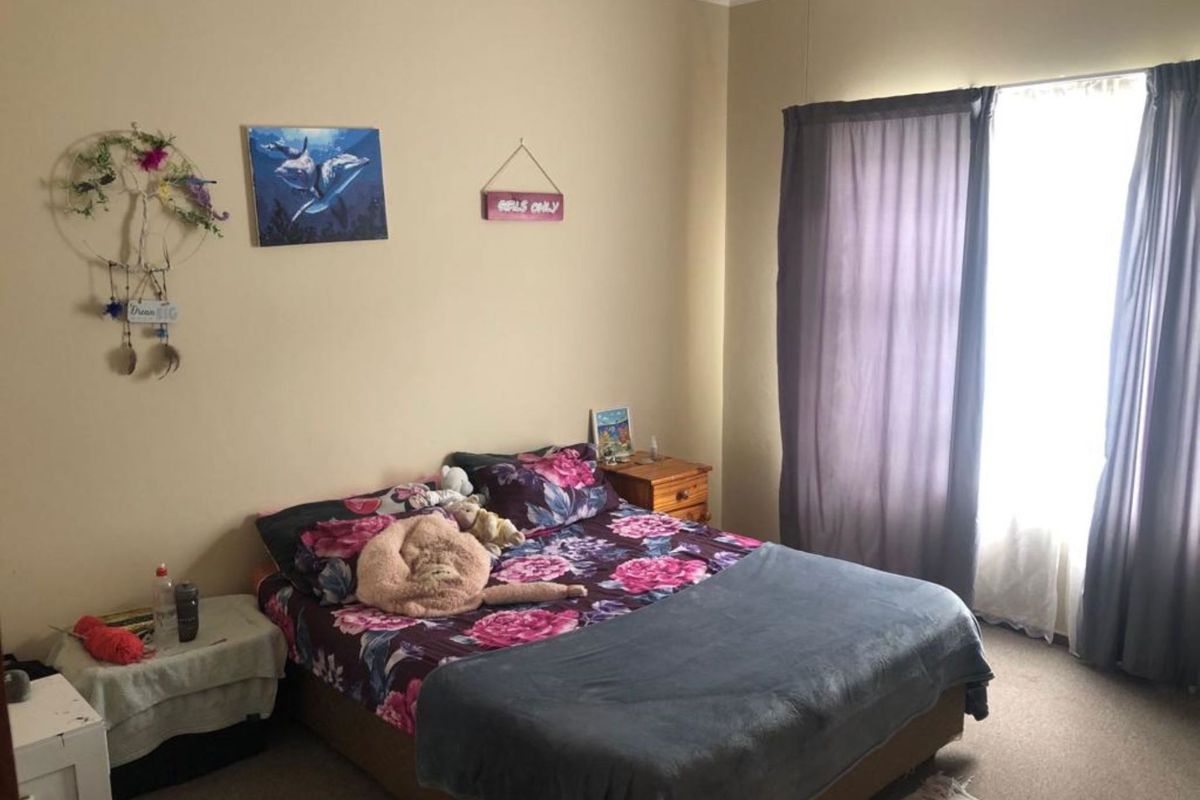 A standard bedroom featuring neutral wall paint, carpeted flooring, and a window with curtains providing natural light.