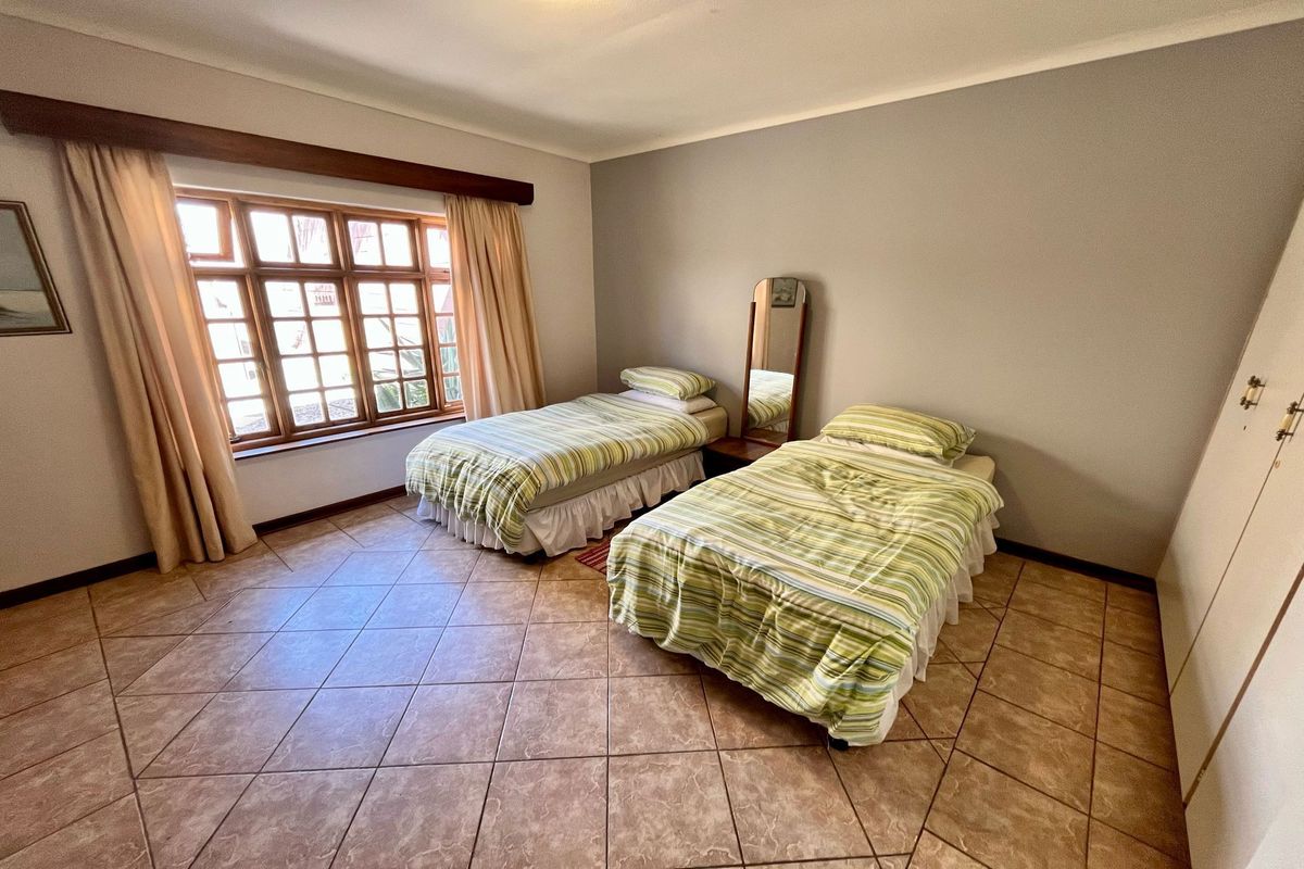 A bedroom featuring tiled flooring, built-in cupboards, and a large wooden-framed window providing natural light.