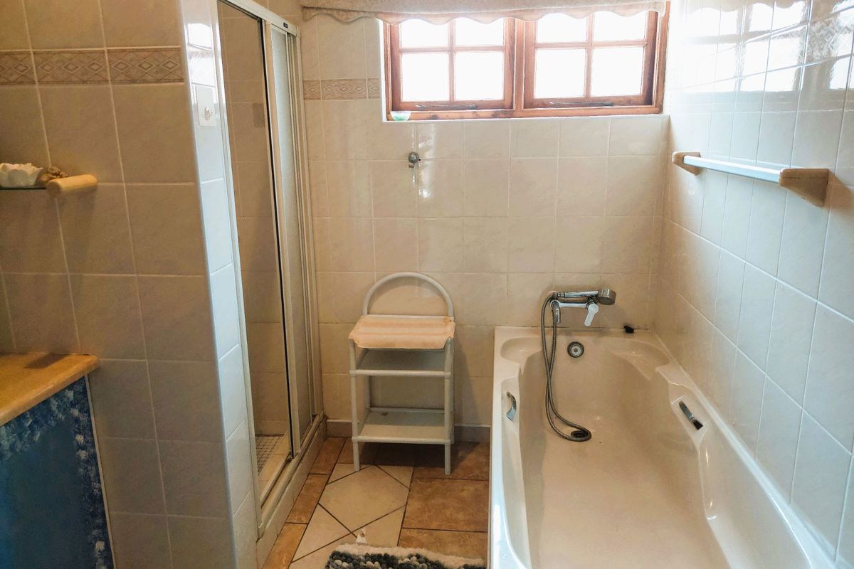A functional bathroom featuring a built-in bathtub with handheld shower attachment, a separate glass-enclosed shower stall, and neutral wall tiling.