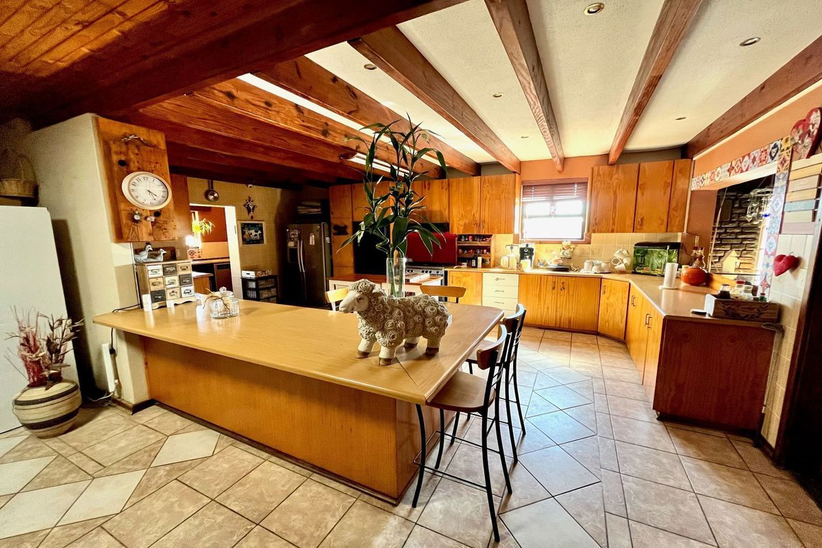 Spacious kitchen featuring timber cabinetry, exposed wooden ceiling beams, a large breakfast bar, and tiled flooring.