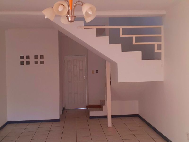 An open-plan living area featuring tiled flooring, a central staircase, and a glass block feature wall, providing a blank canvas for interior design.