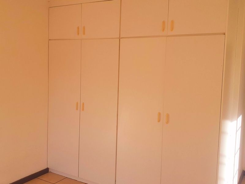 A clean, empty bedroom featuring neutral tiled flooring and ample built-in storage cupboards.