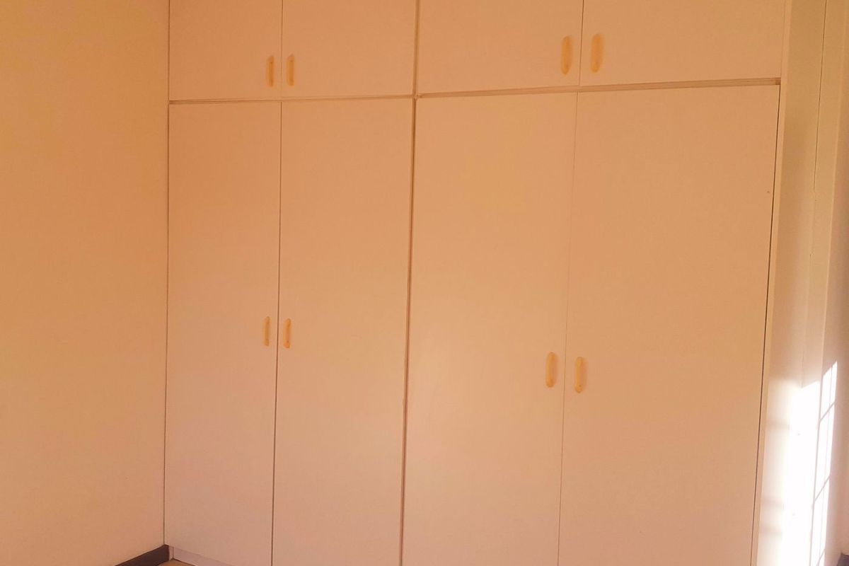 A clean, empty bedroom featuring neutral tiled flooring and ample built-in storage cupboards.