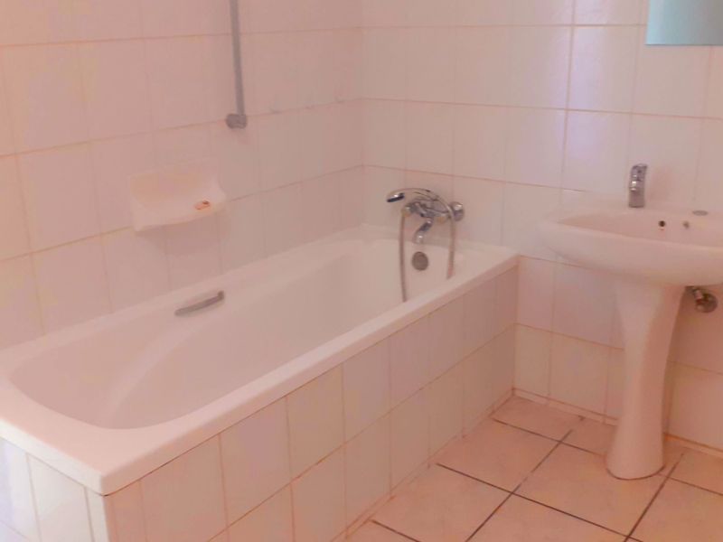 A dated bathroom featuring a standard bathtub, pedestal basin, and tiled finishes, offering a blank canvas for modern renovation.