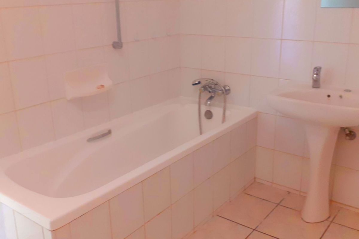 A dated bathroom featuring a standard bathtub, pedestal basin, and tiled finishes, offering a blank canvas for modern renovation.