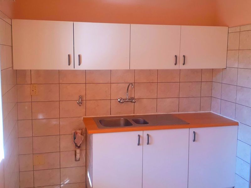 A compact kitchen area featuring white built-in cabinetry, a stainless steel sink, and tiled wall finishes.