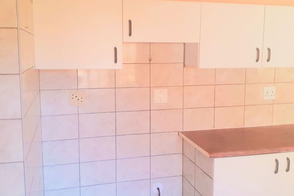 A basic kitchen area featuring white built-in cabinetry, laminate countertops, and tiled walls, currently requiring minor finishing and electrical maintenance.