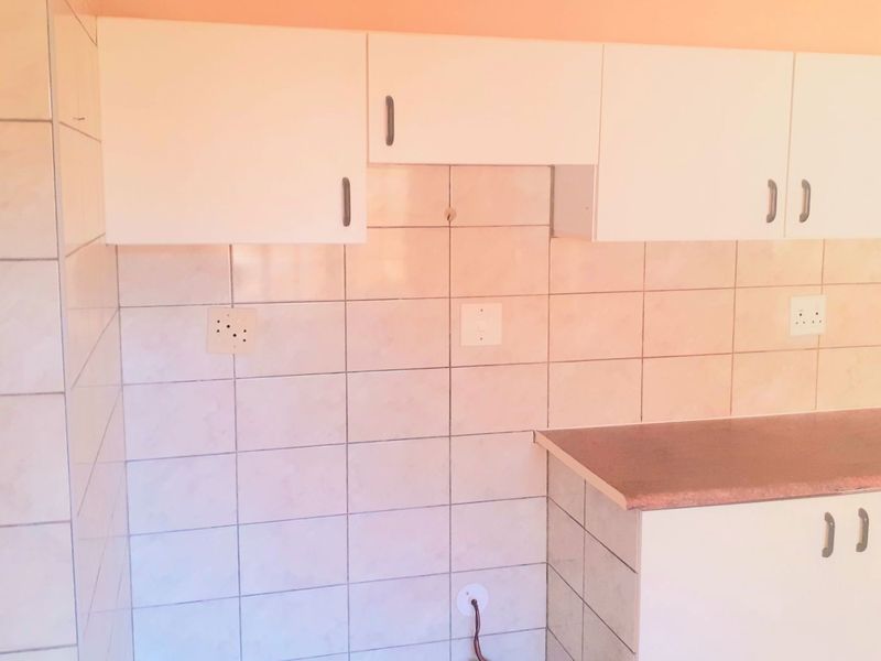 A basic kitchen area featuring white built-in cabinetry, laminate countertops, and tiled walls, currently requiring minor finishing and electrical maintenance.