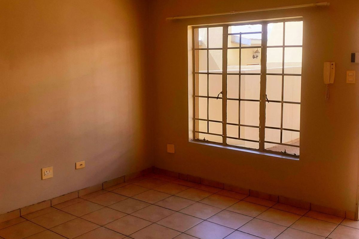 An empty bedroom featuring tiled flooring, a large window with security bars, and an integrated wall-mounted intercom system.
