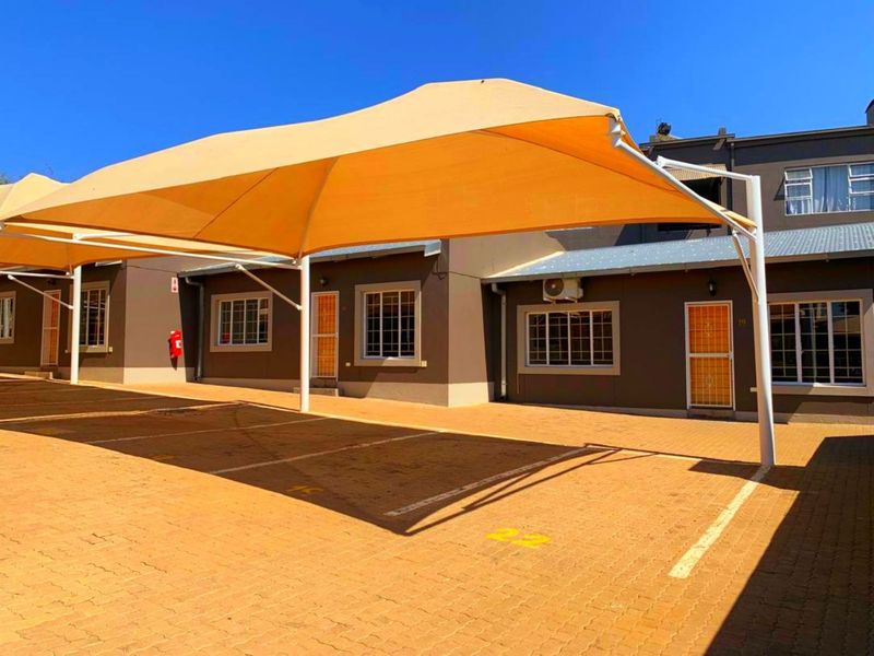 Exterior view of the apartment complex featuring covered parking bays with shade sails, paved driveway, and secure access points.