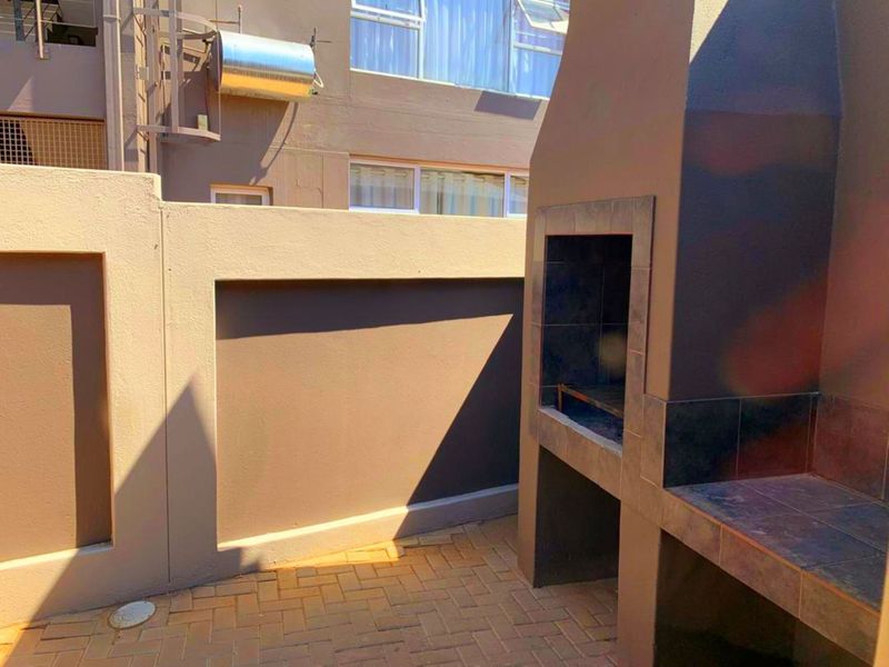 A private outdoor patio area featuring a built-in braai, paved flooring, and a secure boundary wall, ideal for outdoor entertaining.