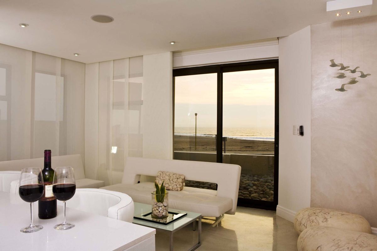 Modern living area featuring sleek finishes, recessed ceiling lighting, and large sliding glass doors offering direct views of the beach and ocean.