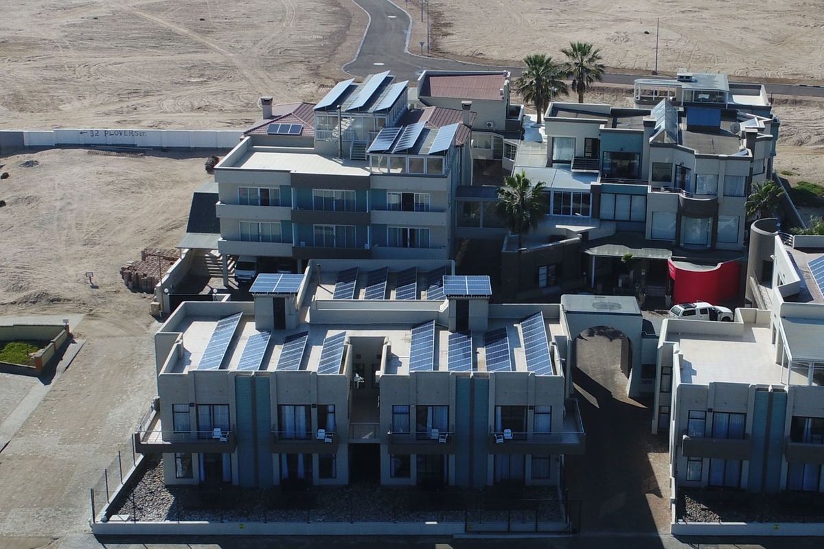 Aerial view of a multi-level guest house complex featuring extensive solar panel installations, flat roof architecture, and paved courtyard areas.