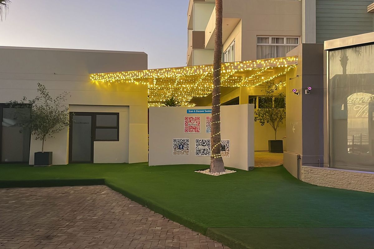 A well-maintained outdoor courtyard area featuring artificial turf, paved driveway, and a covered patio area illuminated with decorative string lighting.
