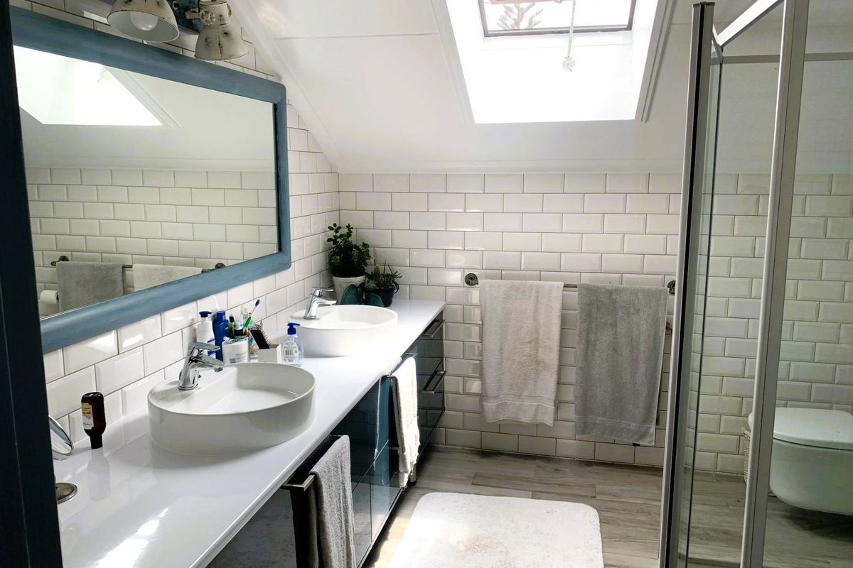 Modern bathroom featuring a double vanity with vessel sinks, subway tile backsplash, glass-enclosed shower, and a skylight providing natural light.