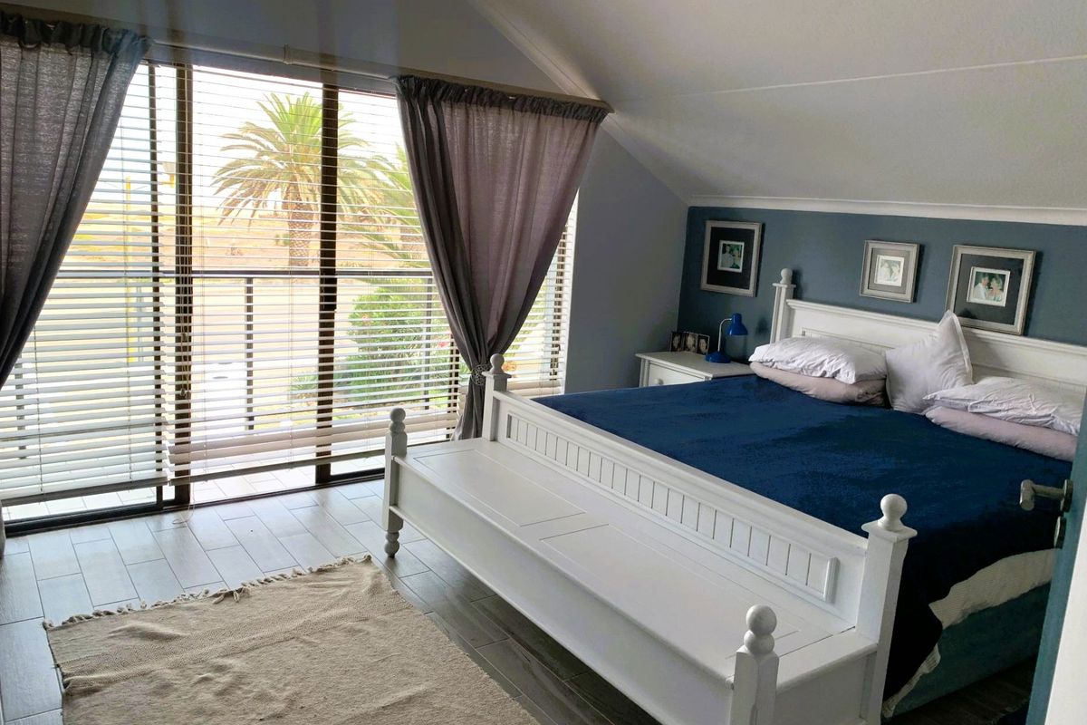 A well-maintained bedroom featuring a vaulted ceiling, tiled flooring, and large sliding glass doors that provide access to a balcony with outdoor views.
