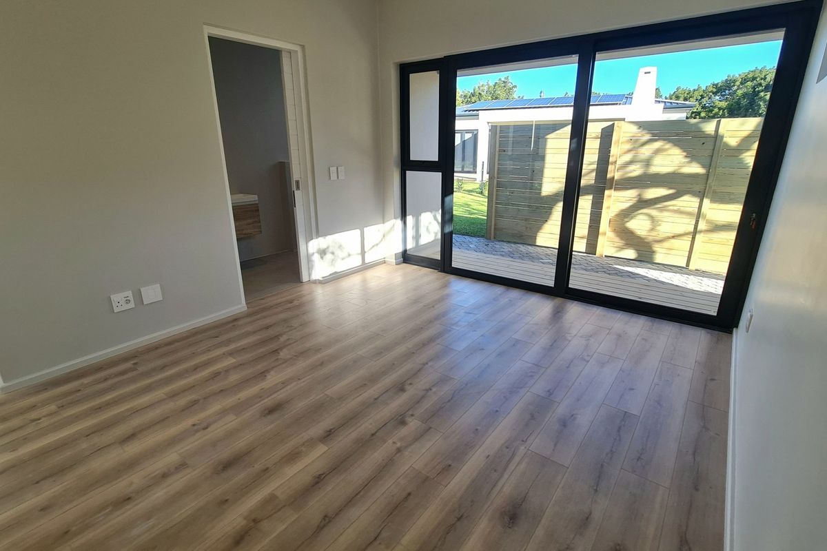 A bright, modern bedroom featuring wood-look laminate flooring, large sliding glass doors leading to a patio, and an adjoining en-suite bathroom.