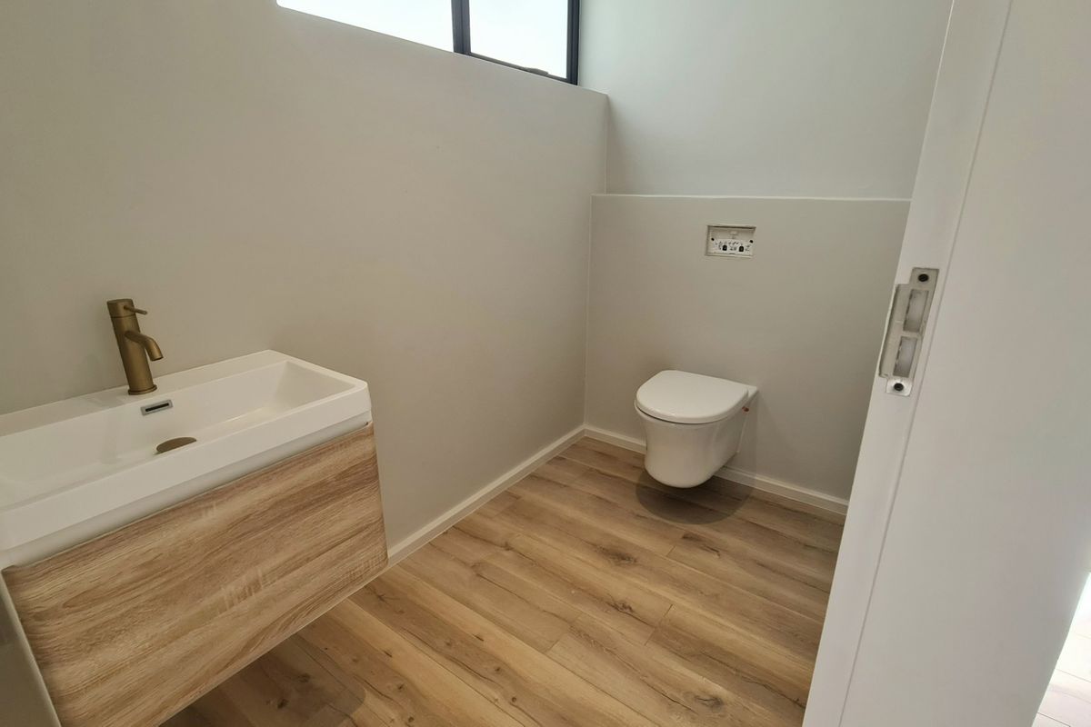 A modern, minimalist powder room featuring a wall-mounted toilet, a contemporary vanity with a brass faucet, and wood-look flooring.