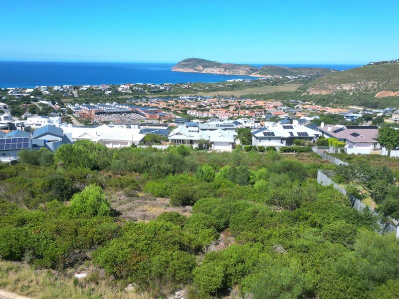 An elevated aerial view of a vacant residential plot overlooking a coastal town, ocean, and surrounding landscape.