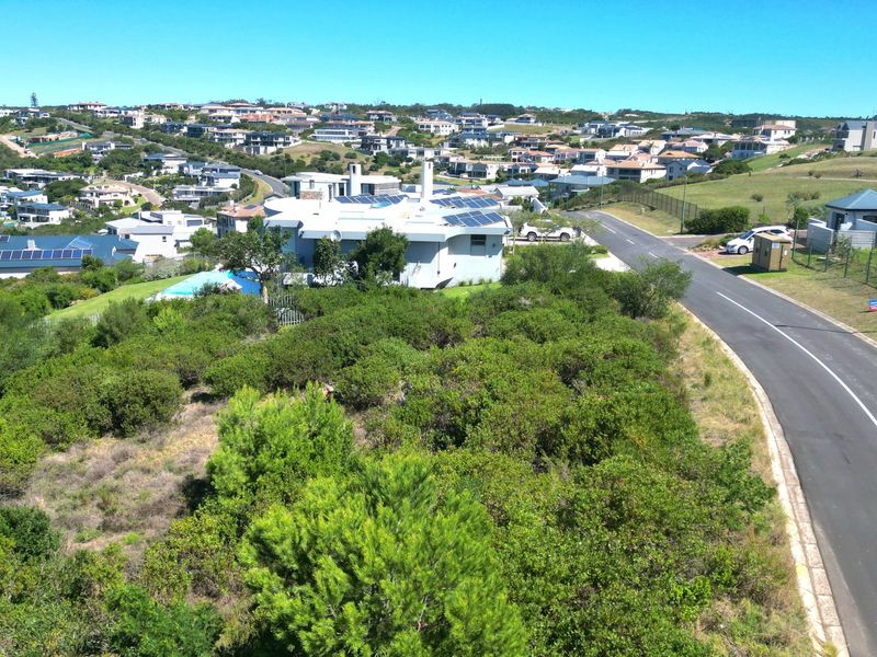 An aerial view of a vacant residential plot situated in a developed estate, featuring established road access and surrounding natural vegetation.
