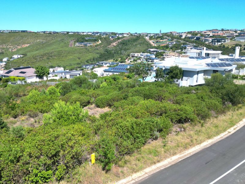 An aerial view of a vacant residential plot situated within a developed estate, featuring native vegetation and adjacent paved road access.