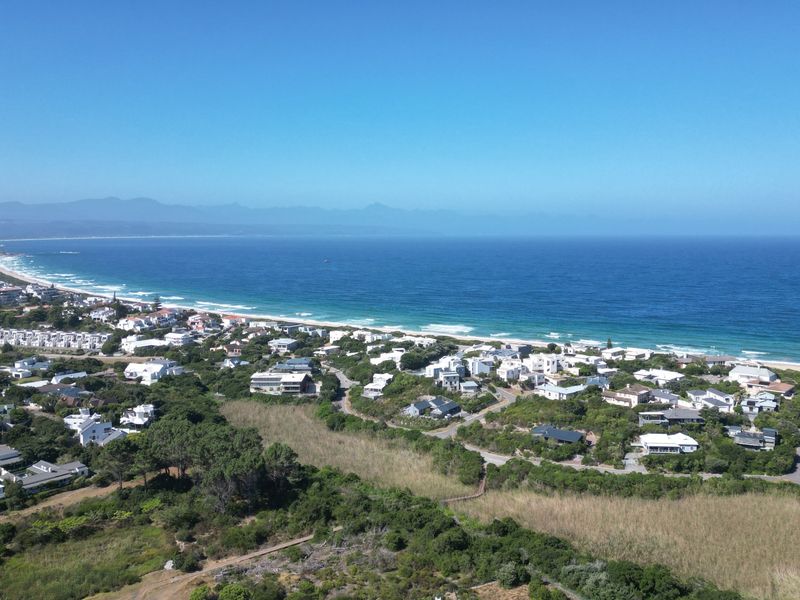 An elevated aerial view showcasing the coastal residential neighborhood, surrounding natural vegetation, and proximity to the ocean and beach.