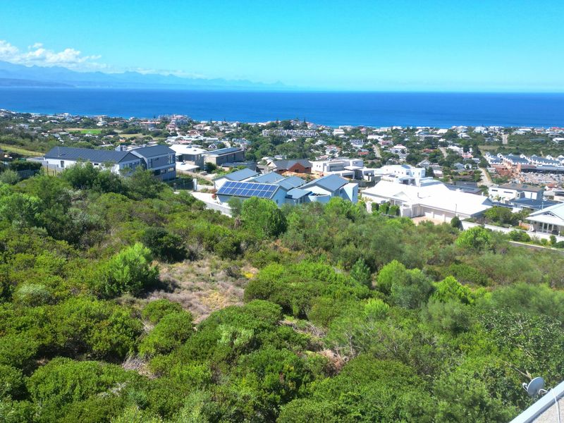 An elevated view overlooking a coastal residential neighborhood with expansive ocean and mountain vistas.