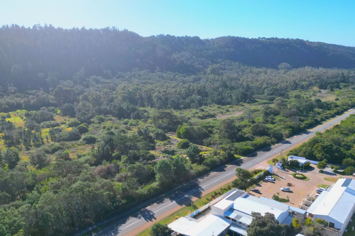 Aerial view of the vacant land parcel adjacent to a main road, surrounded by dense natural vegetation and nearby commercial infrastructure.