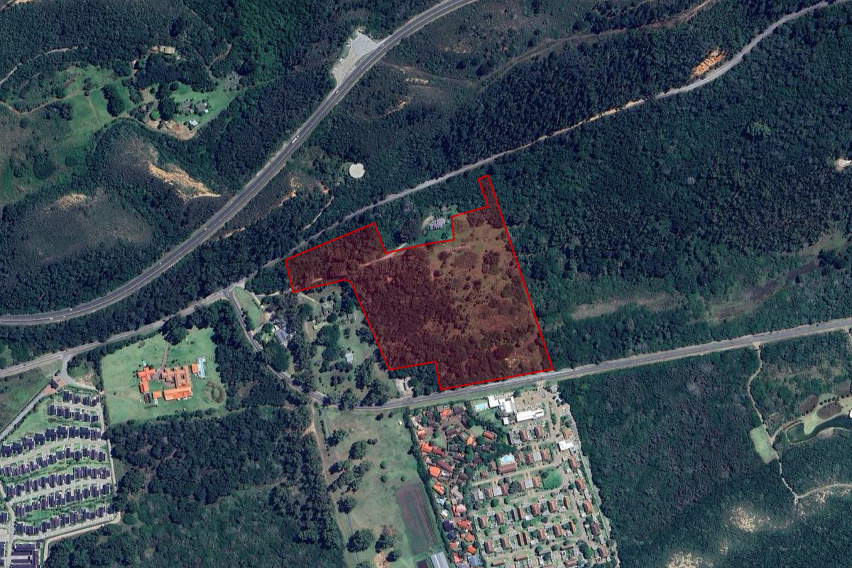 An aerial view showing the boundaries of a large, undeveloped residential plot surrounded by dense forest and nearby suburban infrastructure.