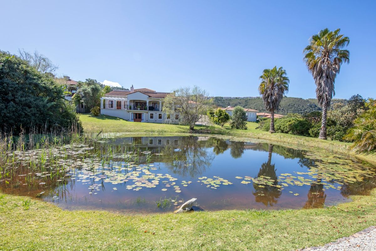 A scenic view of a residential property featuring a tranquil pond, manicured lawn, and mature palm trees in a peaceful estate setting.
