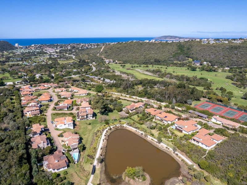 Aerial view of a residential estate featuring a lake, golf course, and tennis courts, set within a scenic coastal landscape.