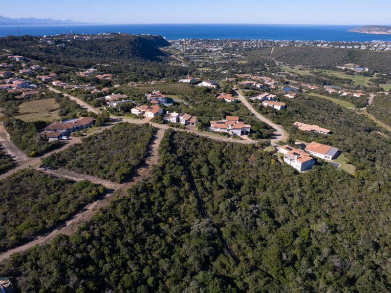 An aerial view of a residential estate nestled in a coastal landscape with established vegetation and road infrastructure.