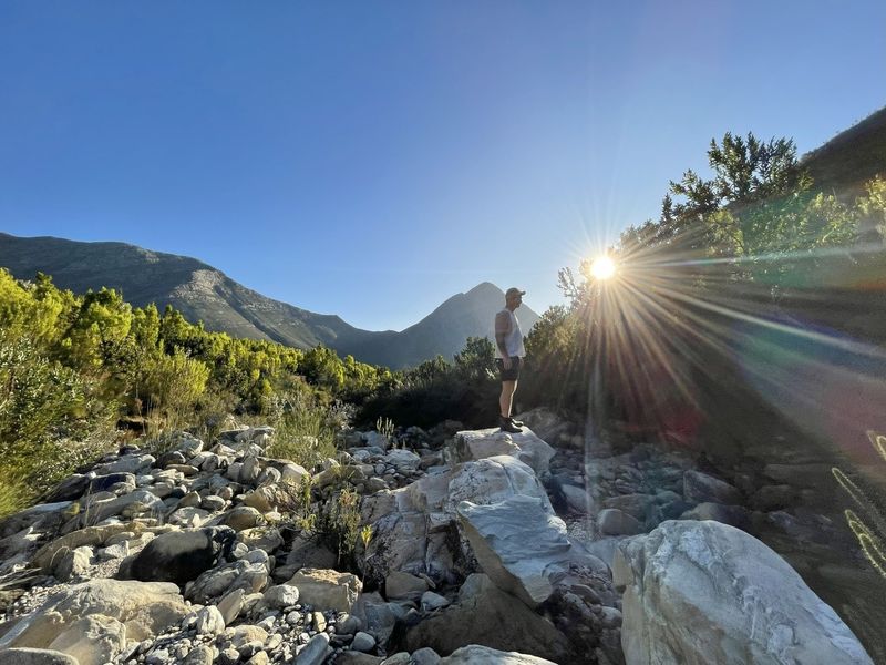 A scenic view of a rocky riverbed set against a backdrop of mountains with natural sunlight.