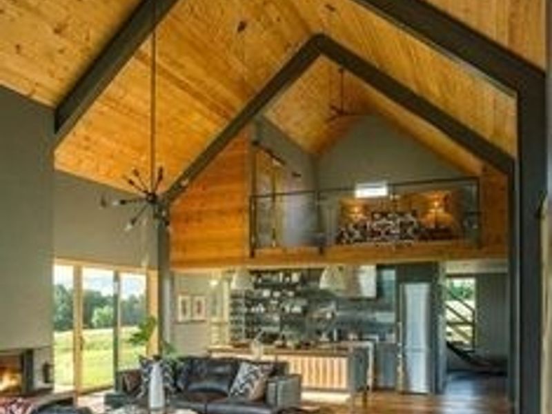 Spacious open-plan living area featuring a dramatic vaulted timber ceiling, exposed steel beams, a mezzanine level, and a modern kitchen with hardwood flooring.