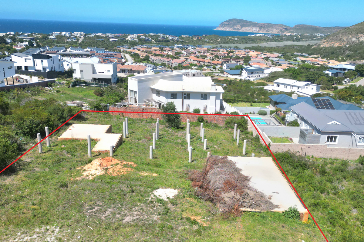 Aerial view of a vacant residential plot featuring concrete foundation piles and a concrete slab, situated in a coastal neighborhood with scenic views.
