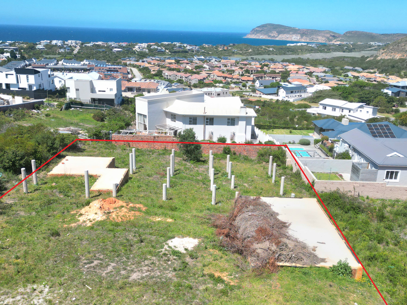 Aerial view of a vacant residential plot featuring concrete foundation piles and a concrete slab, situated in a coastal neighborhood with scenic views.