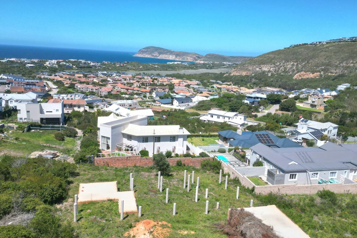 Aerial view of a residential estate featuring a vacant plot with prepared concrete foundation pillars and a slab, overlooking the surrounding coastal neighborhood.