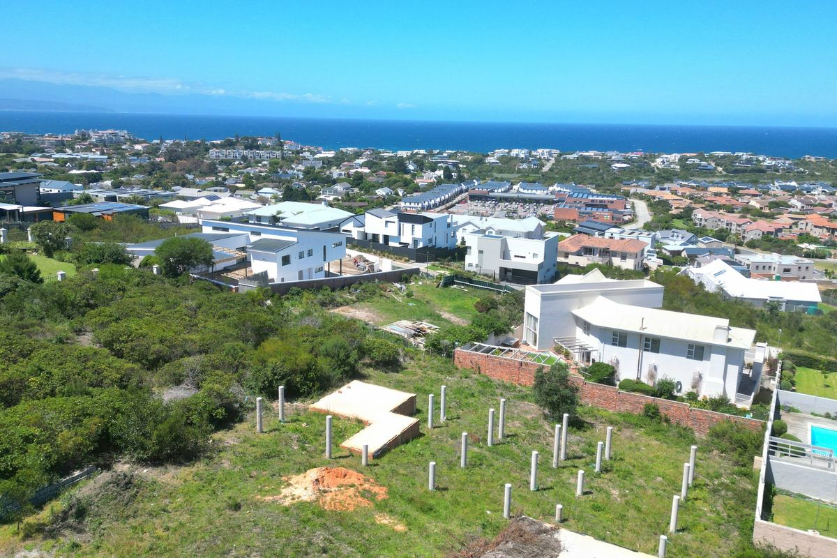 Aerial view of a residential plot featuring exposed concrete foundation piles and a retaining wall, set within a coastal neighborhood.