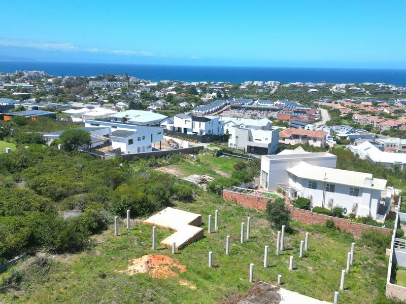 Aerial view of a residential plot featuring exposed concrete foundation piles and a retaining wall, set within a coastal neighborhood.